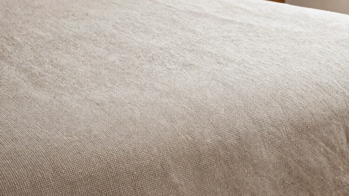 Close natural-light detail of a bedsheet fabric weave on a neutral background, soft daylight, accurate textile texture